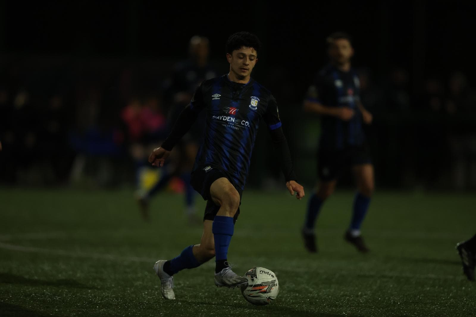 Coach Gabriel Padilla carrying the ball during a night soccer match.