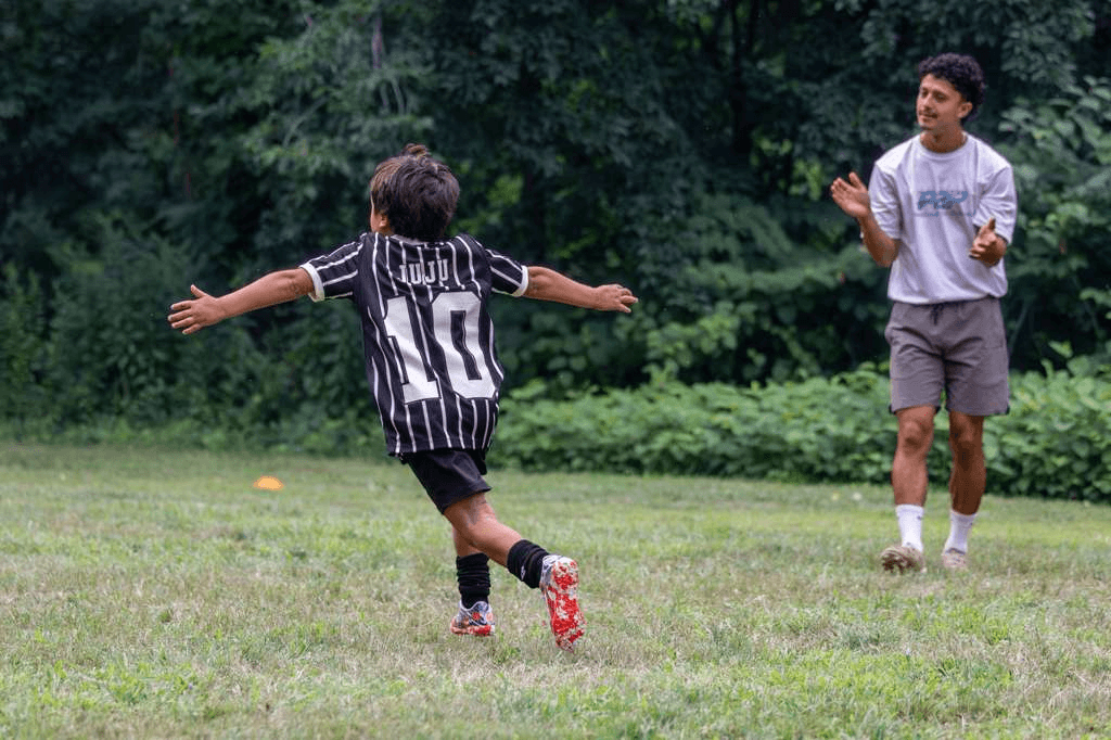 A young P2P soccer player celebrating a finish as Coach Gabriel Padilla applauds.
